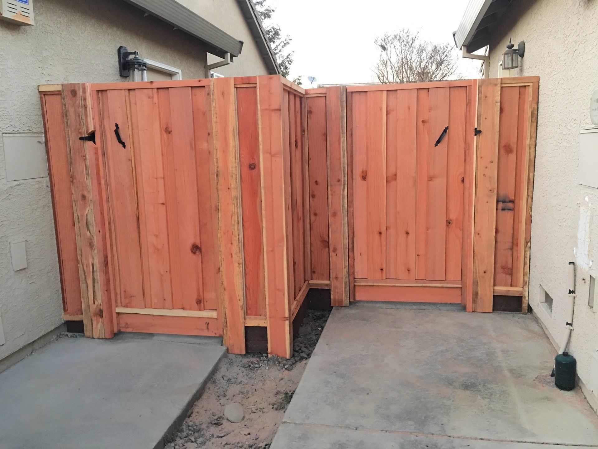 A wooden fence surrounds a concrete walkway in front of a house