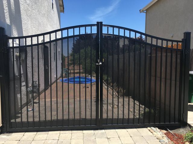 A black gate is sitting in front of a house next to a pool.
