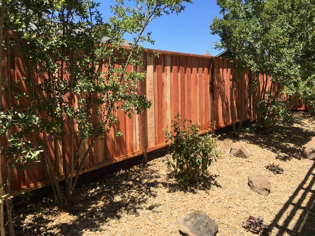 A wooden fence is surrounded by trees and rocks in a backyard.