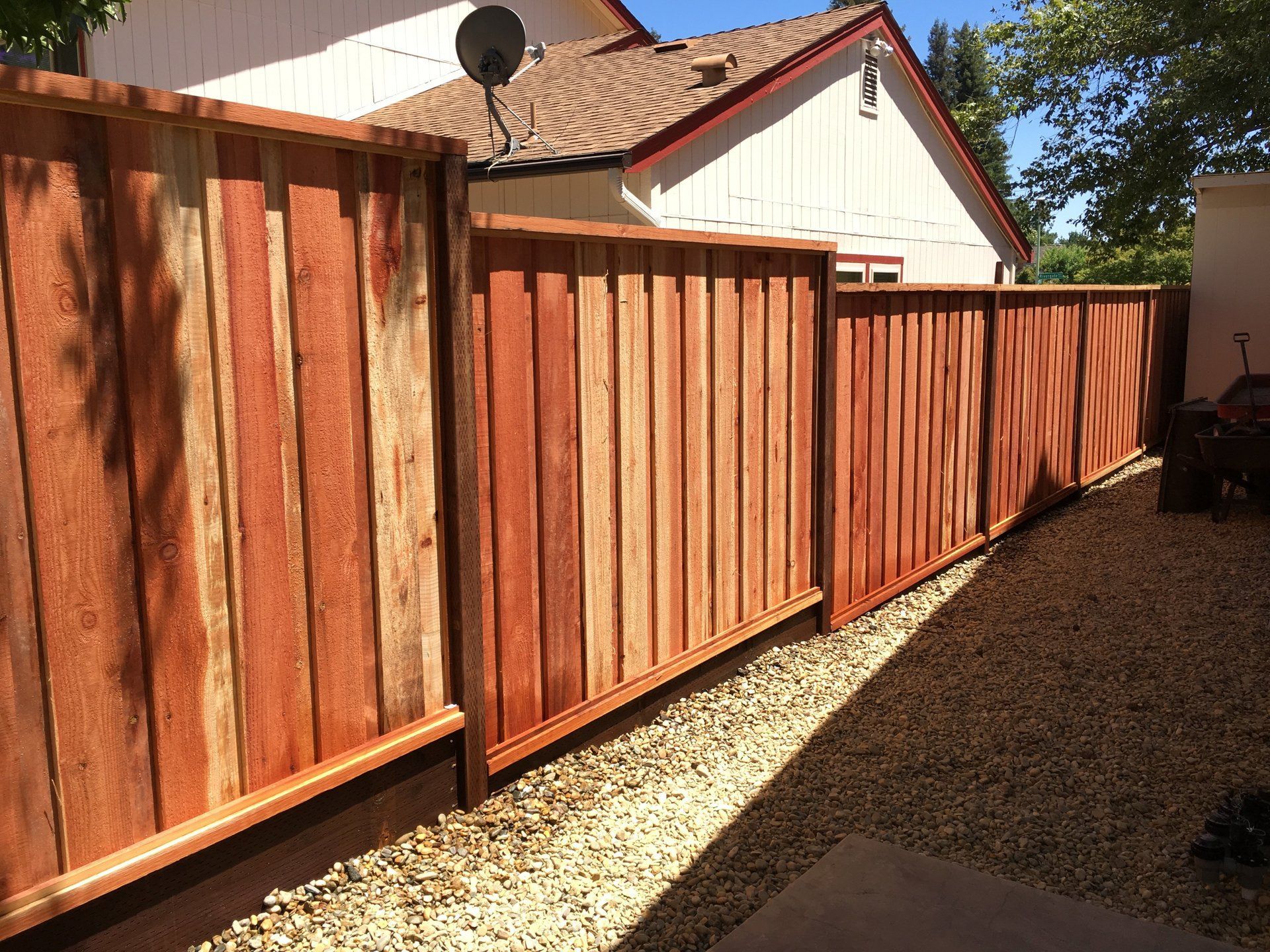 A wooden fence surrounds a gravel area in front of a house.