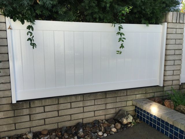 A white fence is sitting on top of a brick wall next to a pool.