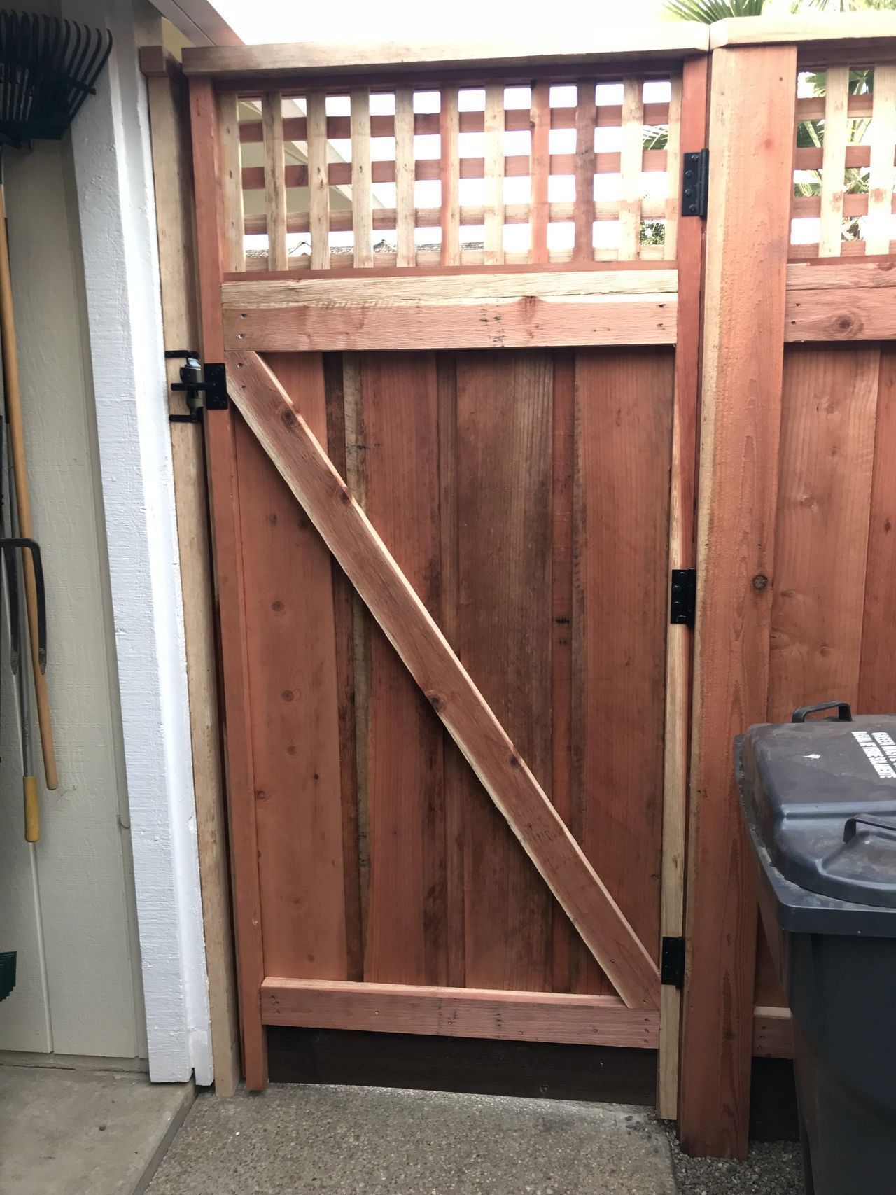 A wooden gate is open next to a trash can.