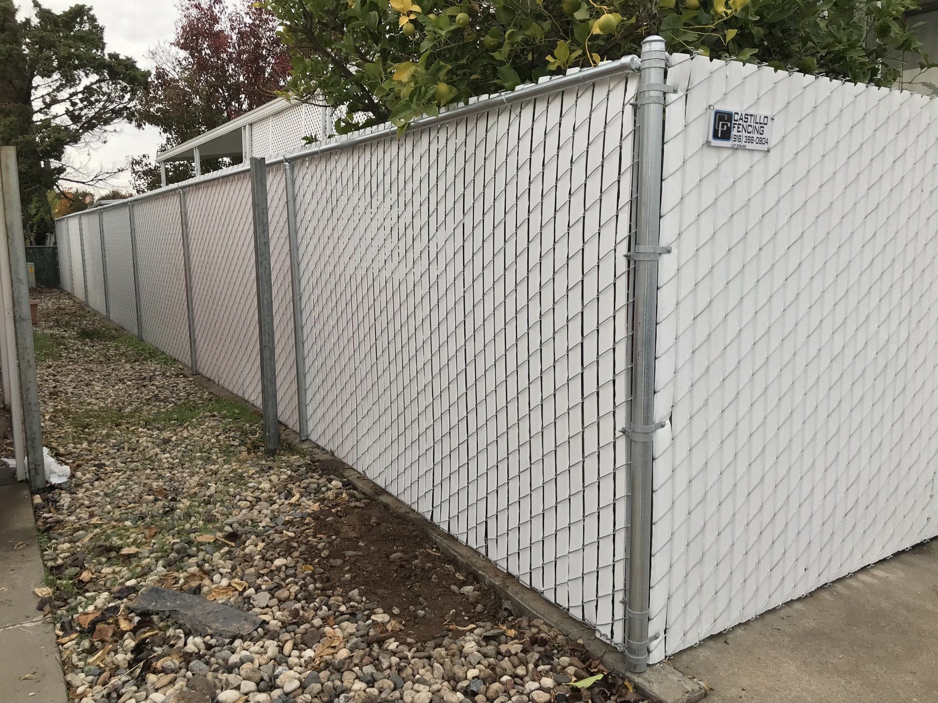 A white chain link fence is sitting next to a sidewalk.