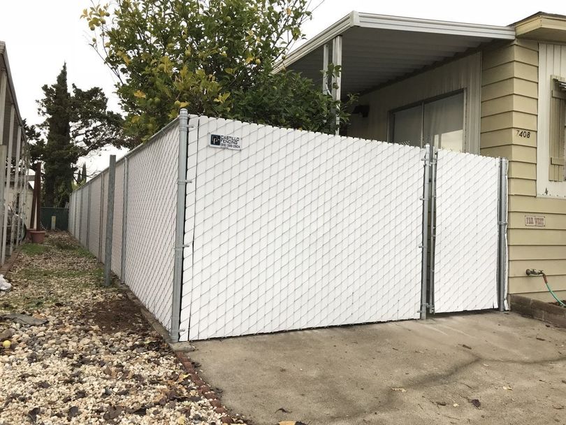 A white chain link fence is in front of a mobile home