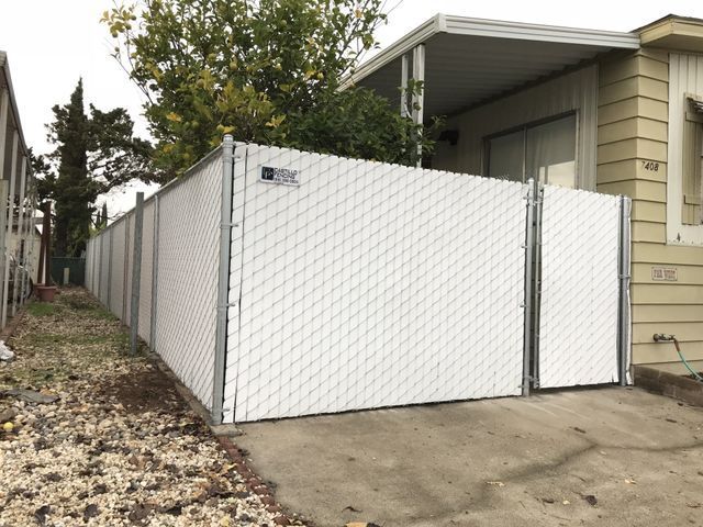 A white chain link fence is in front of a mobile home
