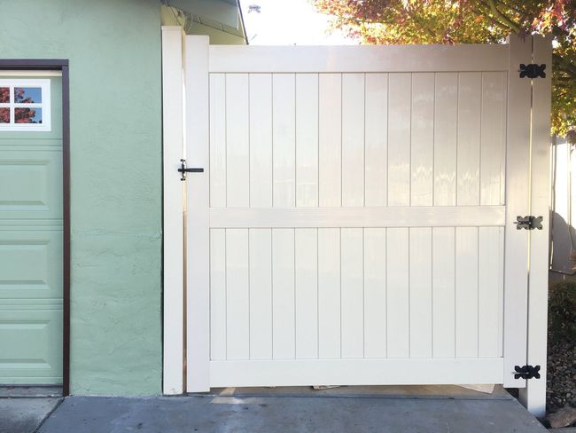 A white gate is sitting next to a green garage door.