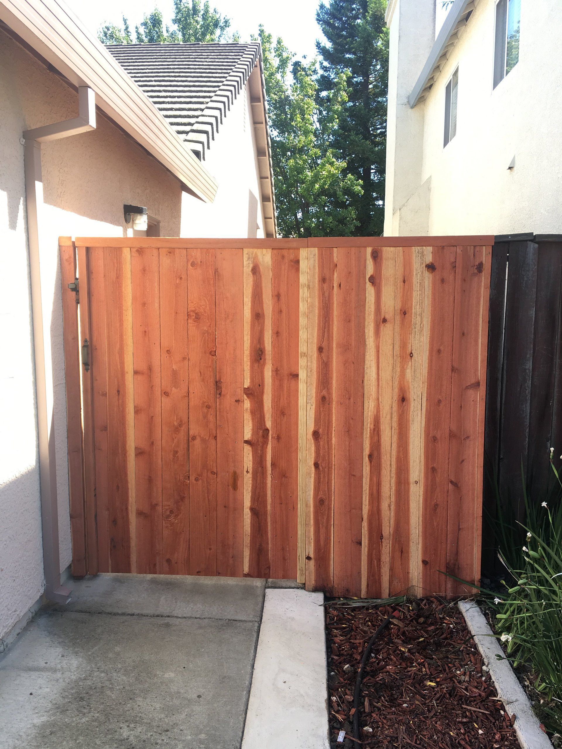 A wooden fence surrounds a driveway leading to a house.