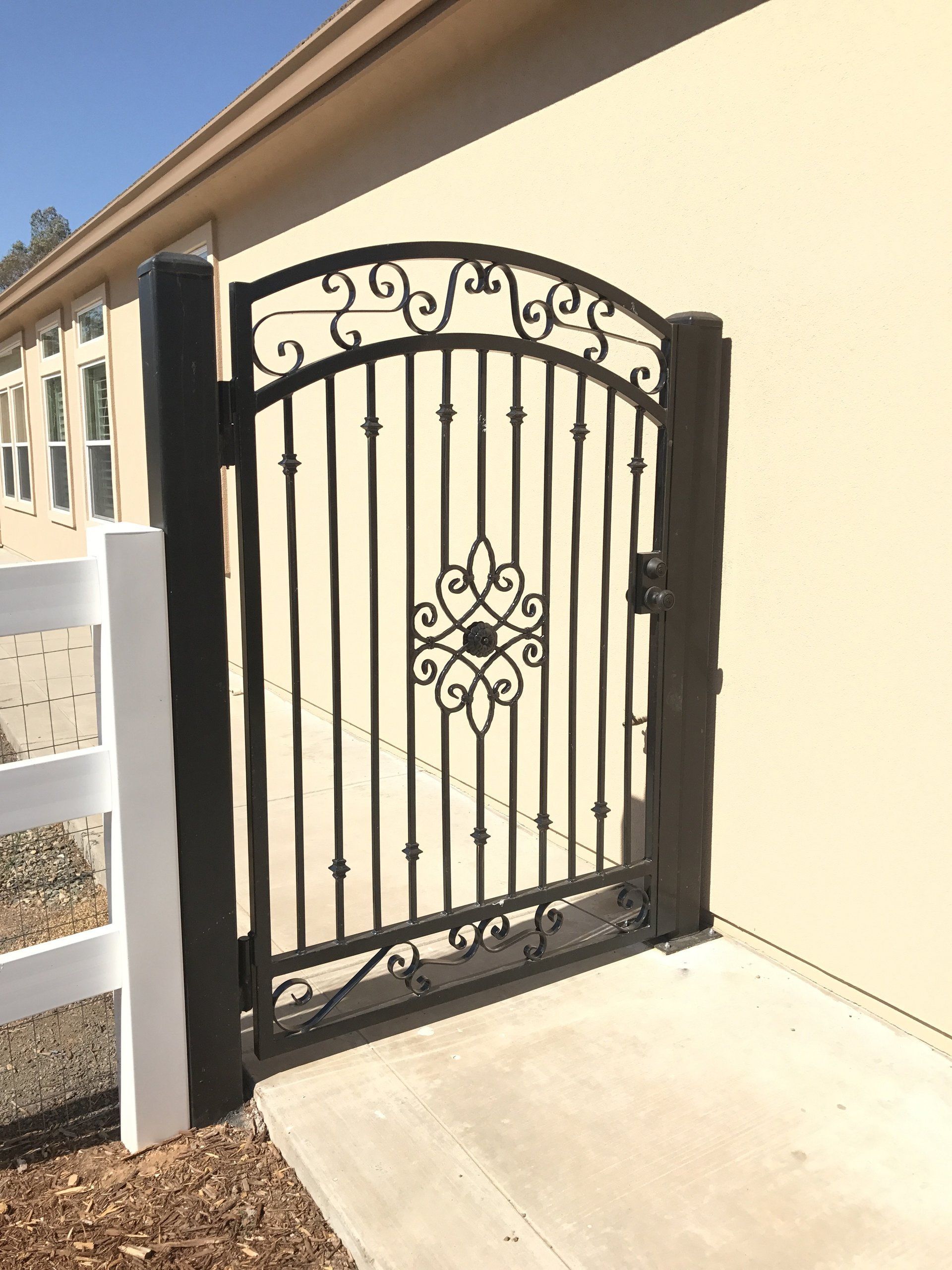A wrought iron gate is sitting next to a white fence.