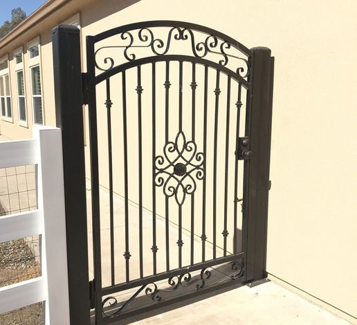 A black wrought iron gate with a white fence in front of a house.