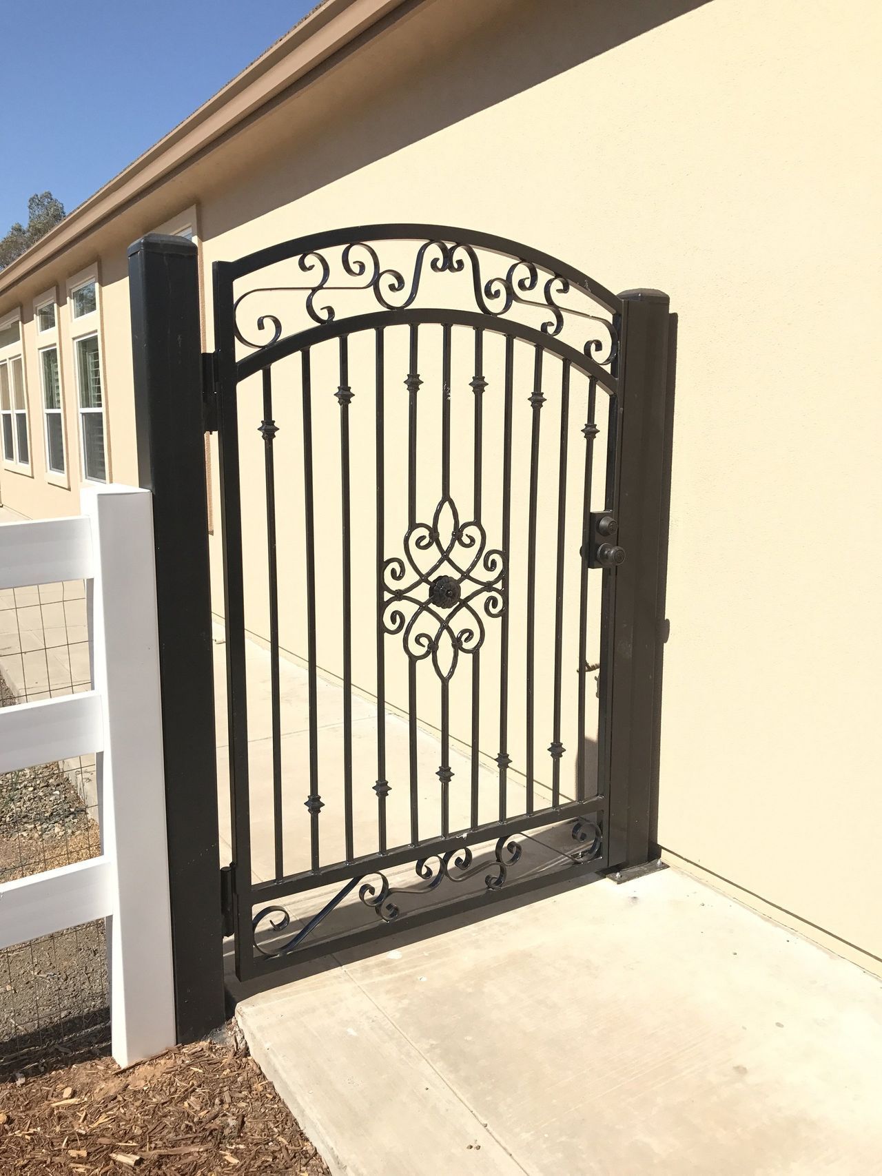 A black wrought iron gate is sitting next to a white fence.