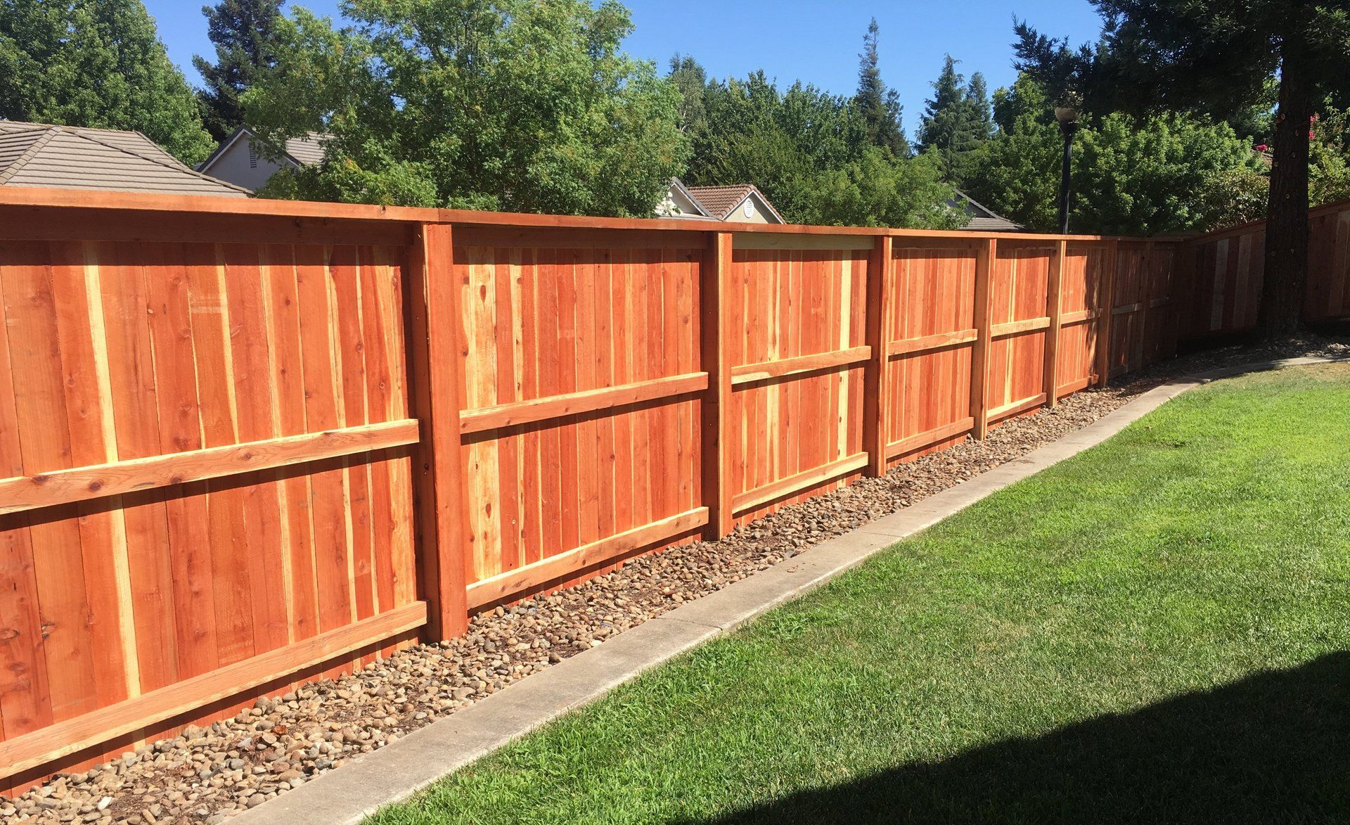 A wooden fence surrounds a lush green lawn in a backyard.