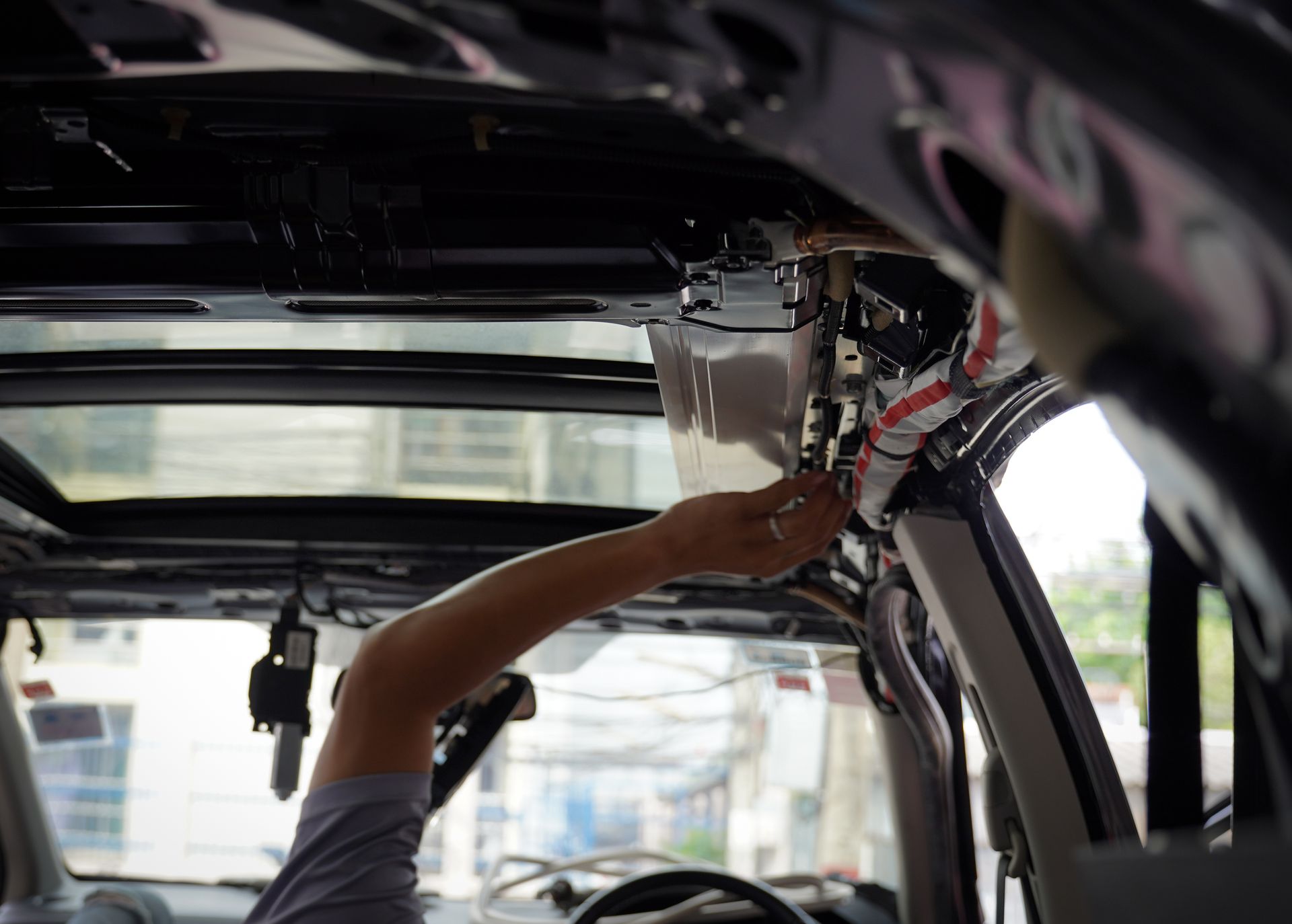 Person working on the interior of a car roof with wiring and sunroof visible.