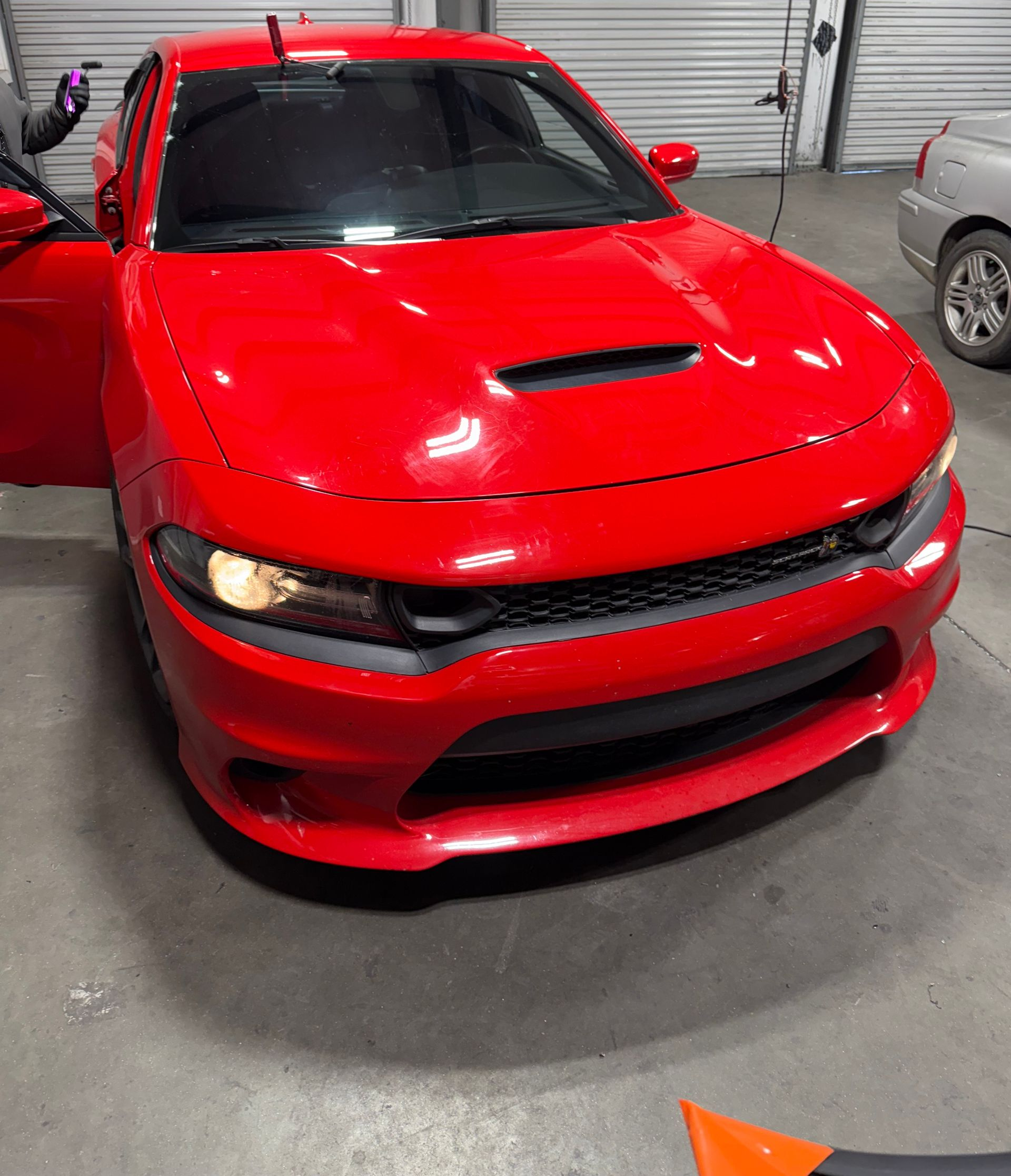 Red Dodge Charger, hood scoop, open door, indoors, garage setting.