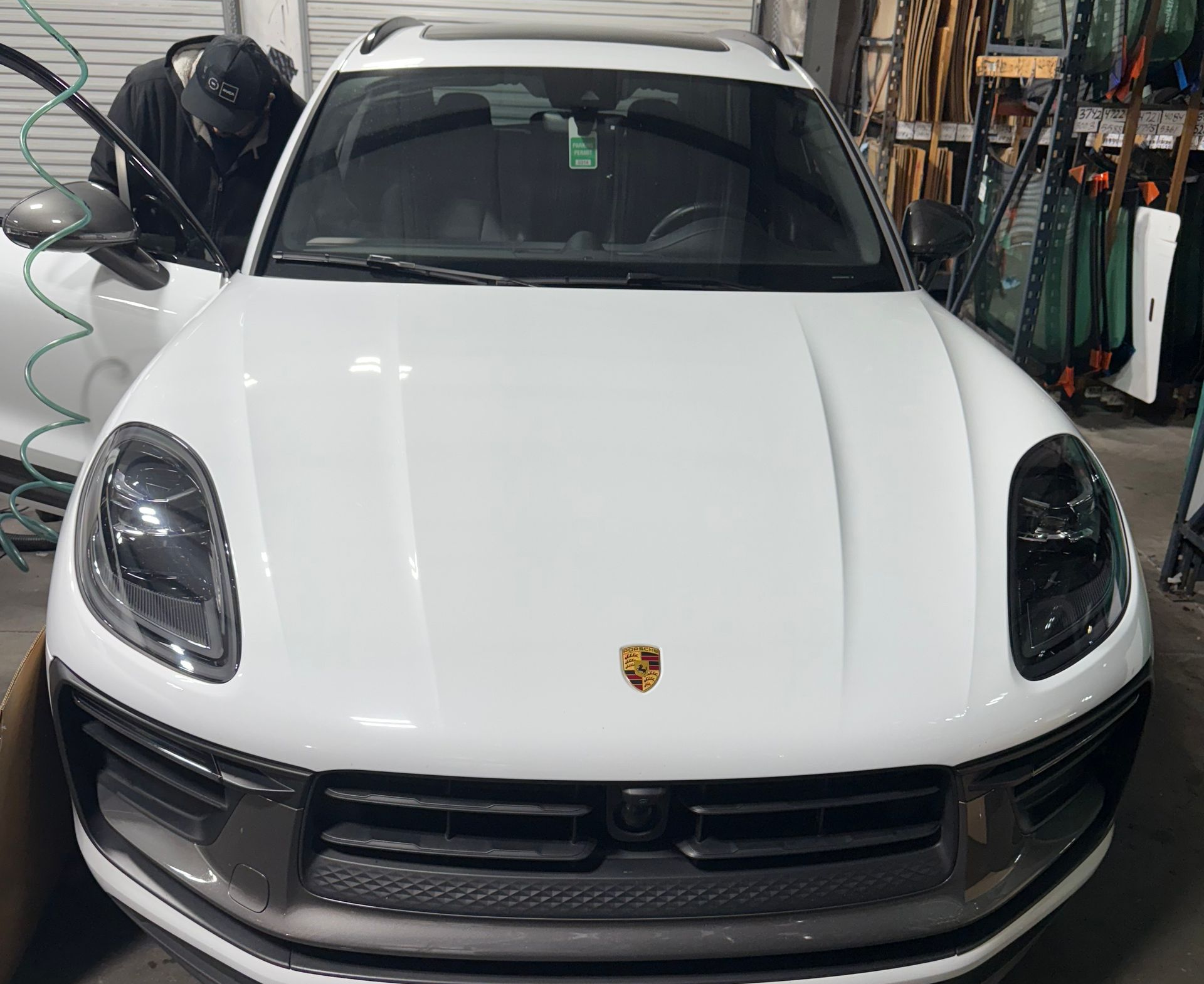 White Porsche Macan SUV in a garage, facing forward. Person in dark clothing by open door.
