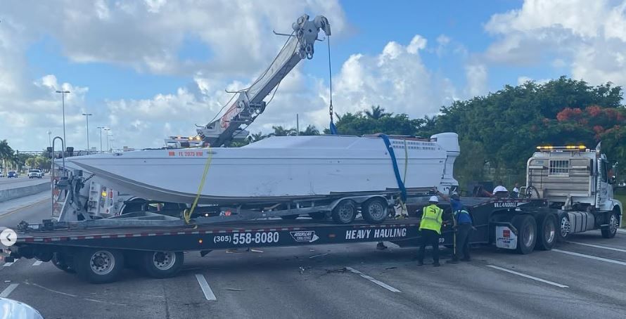 A boat is being towed by a tow truck on a highway.