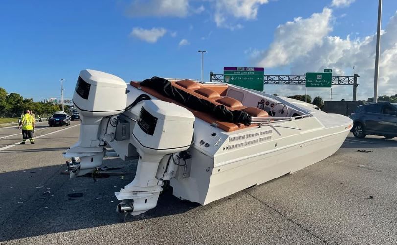 A boat is laying on its side on the side of a highway.