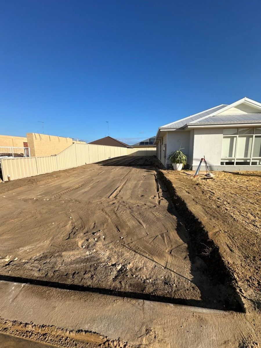 Dirt driveway next to a light-colored house under a clear, blue sky.