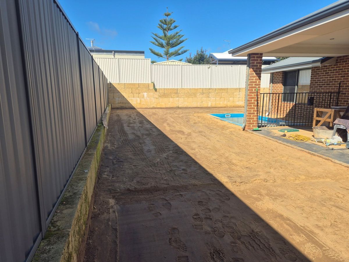 Backyard with sandy ground, gray fence, brick house, and a small pool.