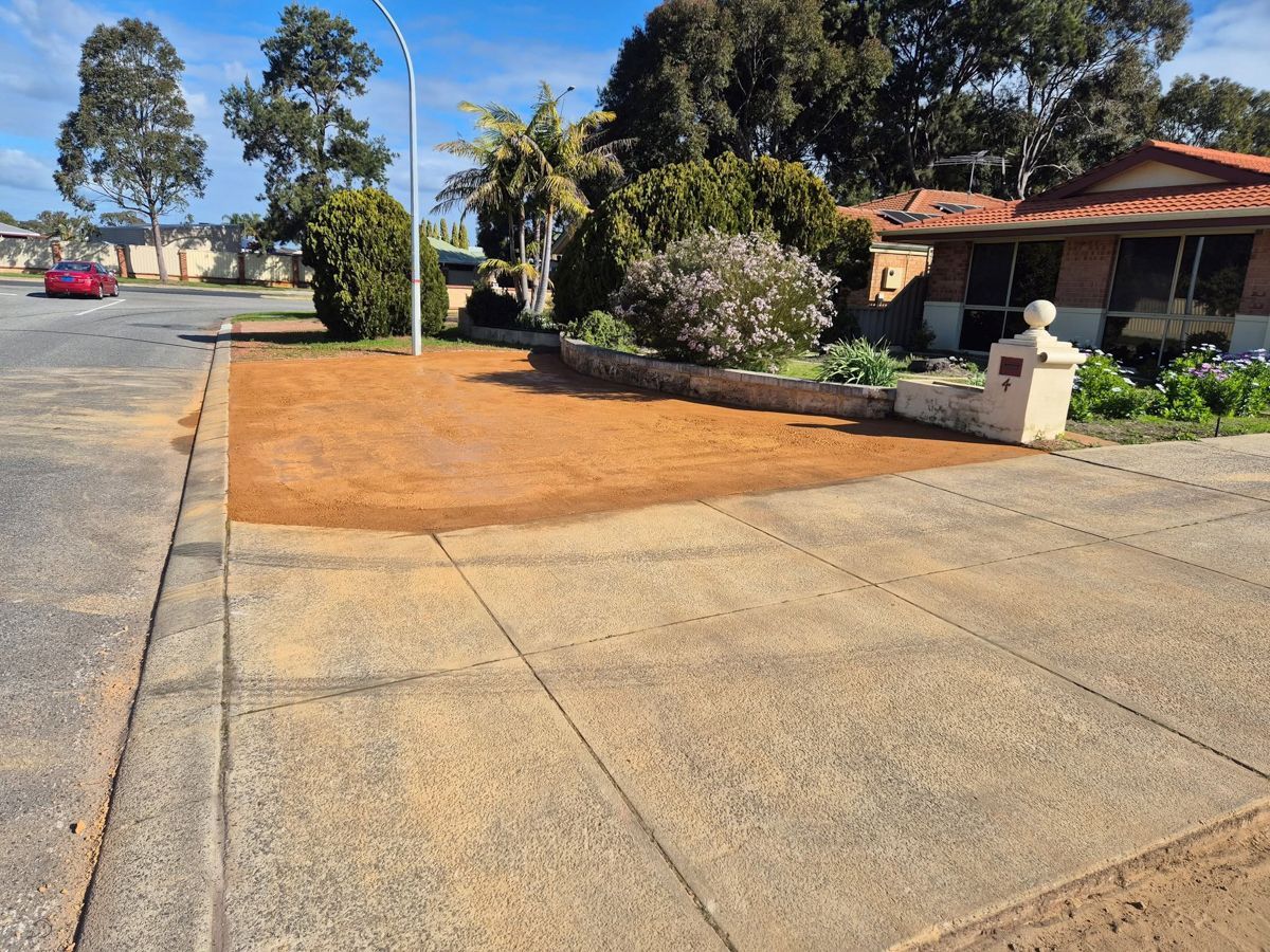 Sidewalk with brown dirt patch in front of a house, a street and houses in the background.