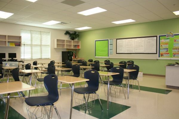 Empty classroom with student desks, green accent wall, and whiteboard.
