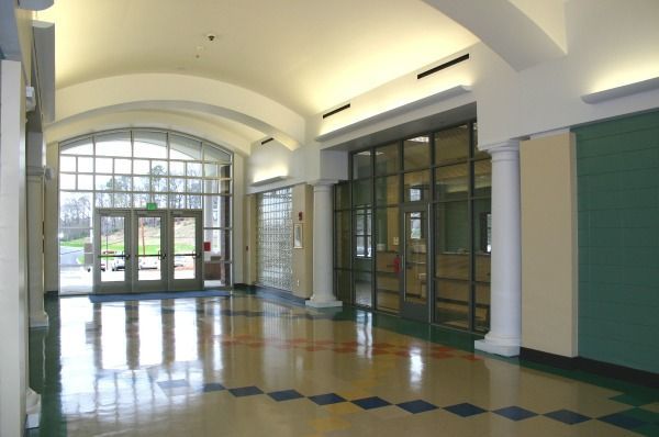 Hallway with glass doors, columns, and checkered floor. Sunlight streams in.
