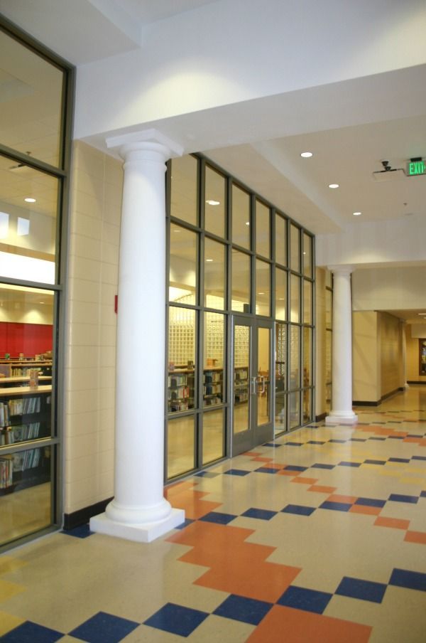 Interior hallway with glass-walled entry, columns, patterned floor, library visible through window.