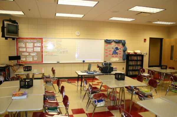 Empty classroom with desks, whiteboard, bulletin boards, and bookshelf.