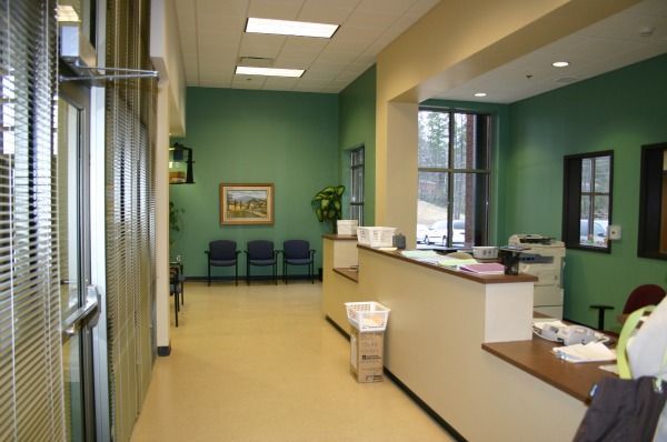 Reception area with light-colored walls, green accent wall, waiting chairs, and a reception desk.