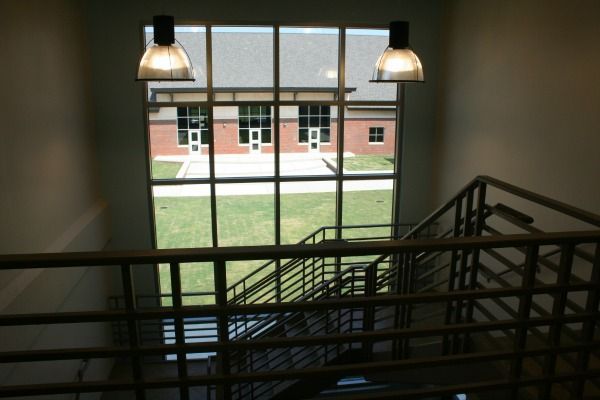 View from stairs, looking out a window at a brick building with green grass. Two hanging lights.