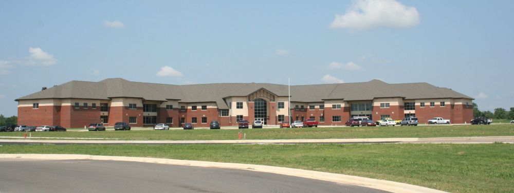 A brick building with a brown roof and vehicles parked in front on a grassy lawn.