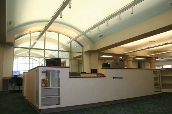 Library interior, check-out desk with computers, large arched window, green carpet.
