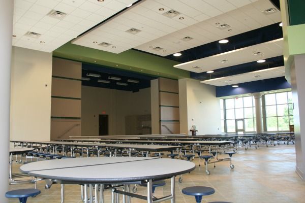 Empty school cafeteria with tables and stage area, blue and green accents.