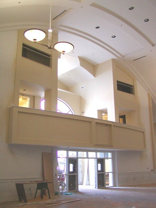 Interior view of a light-filled building under construction, with a balcony overlooking entry doors.