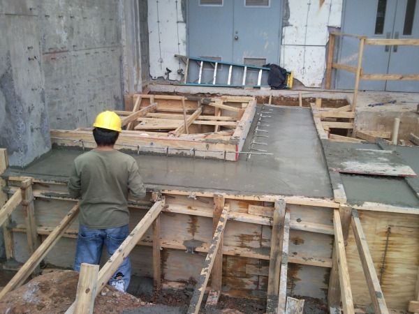 Construction worker smoothing wet concrete on a ramp; wooden forms surround; outdoors.
