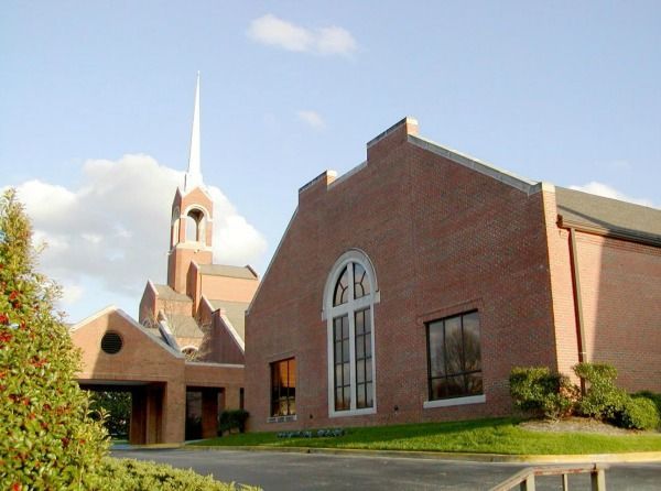 Brick church building with tall steeple, blue sky, and green lawn.