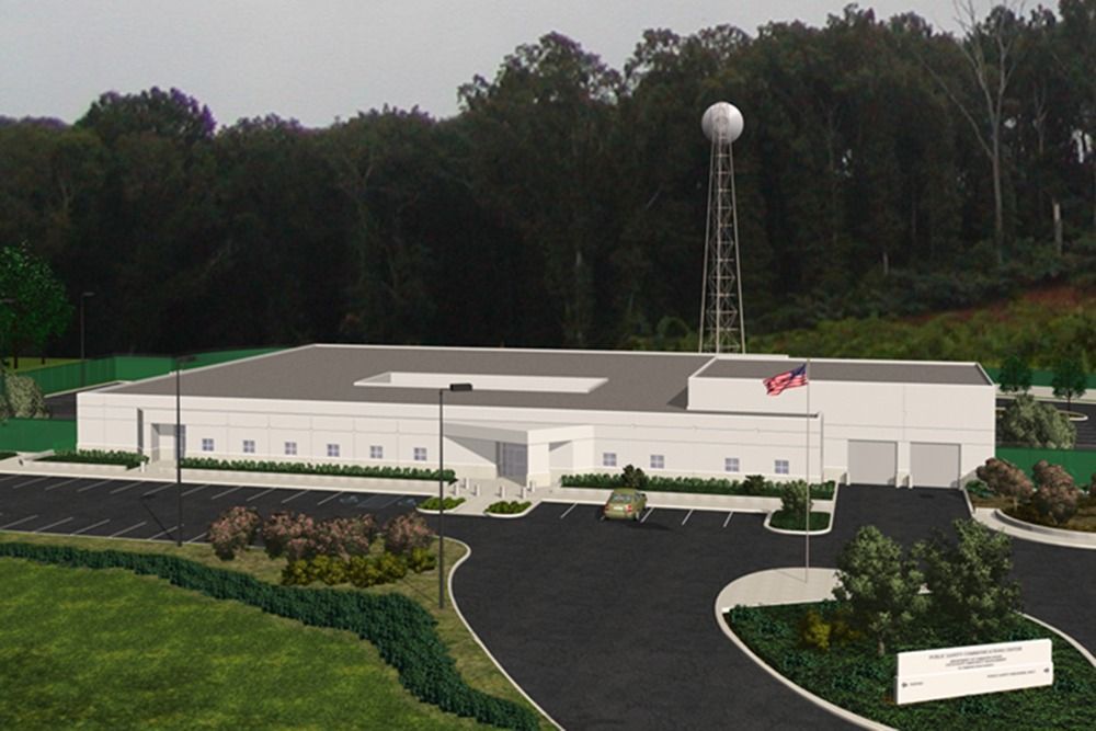 Building with a water tower, parked vehicles, and landscaping against a backdrop of trees.