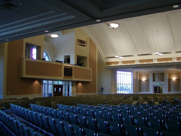 Auditorium interior with rows of blue seats, a stage area, and arched ceiling.