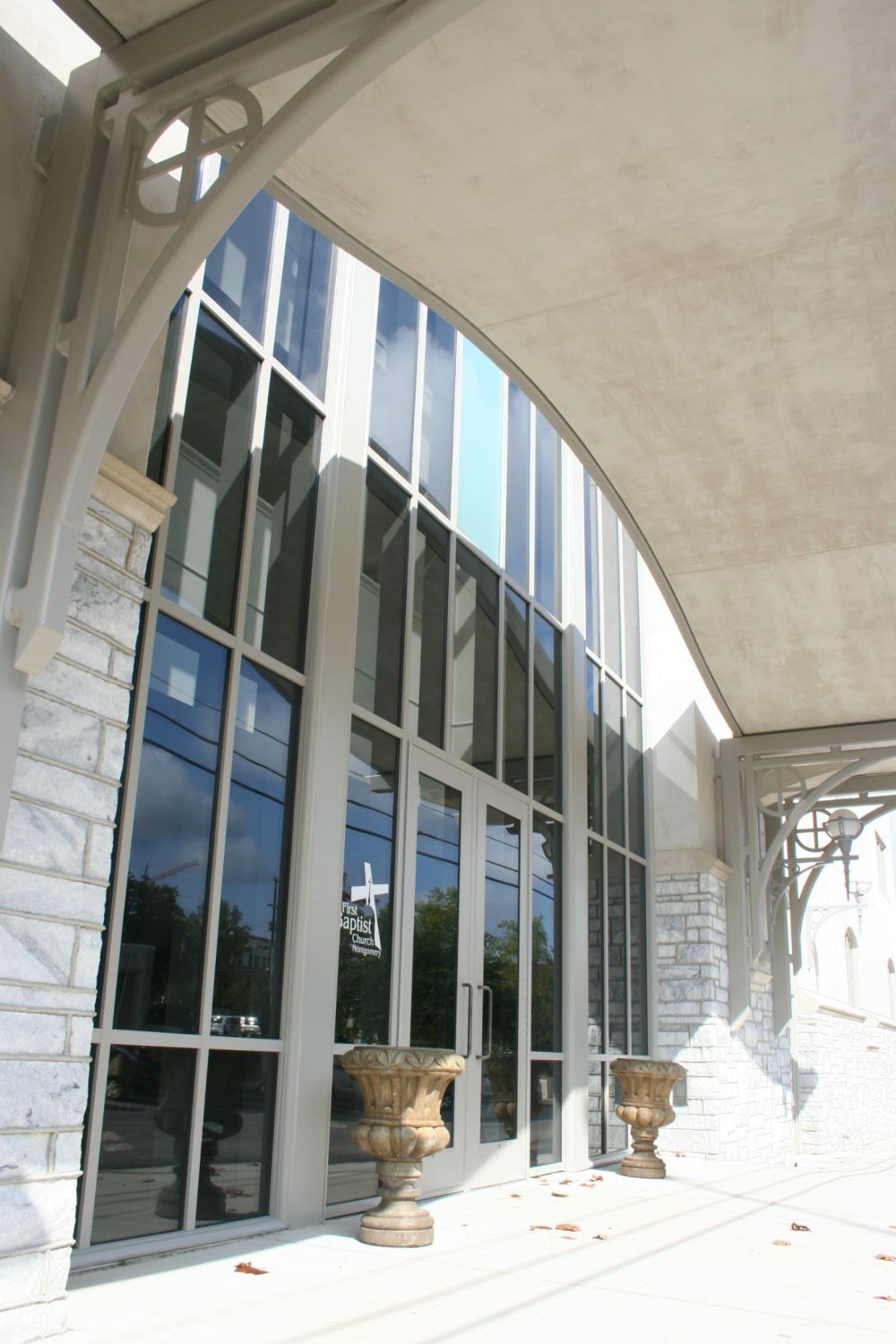 Building facade with tall arched windows, stone accents, and two urns; under a covered walkway.