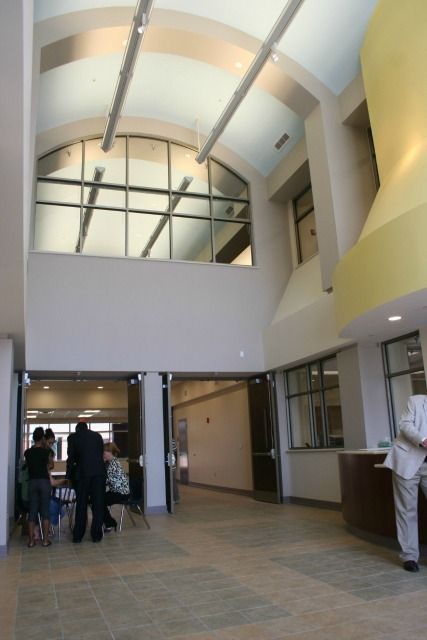 Interior of a building: people near doors and reception desk; arch window; cream walls; tan floor.