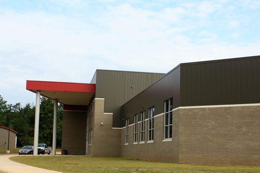 Exterior of a modern building with a red overhang supported by white columns, brick and dark gray siding.