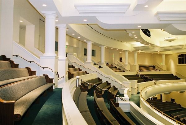 Auditorium with tiered seating, curved balconies, white columns, and pale green carpet.