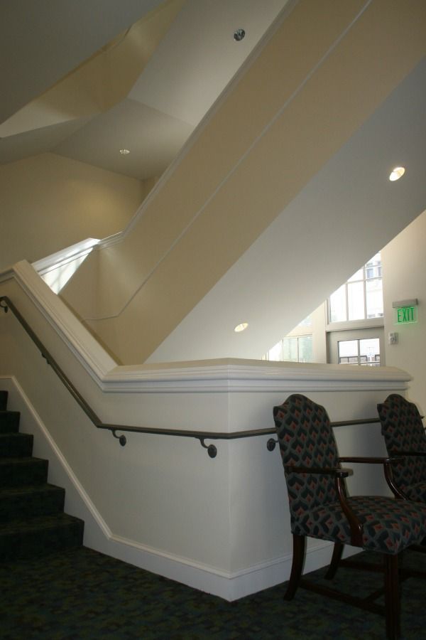 Staircase with white walls and handrails. Two patterned chairs sit nearby.