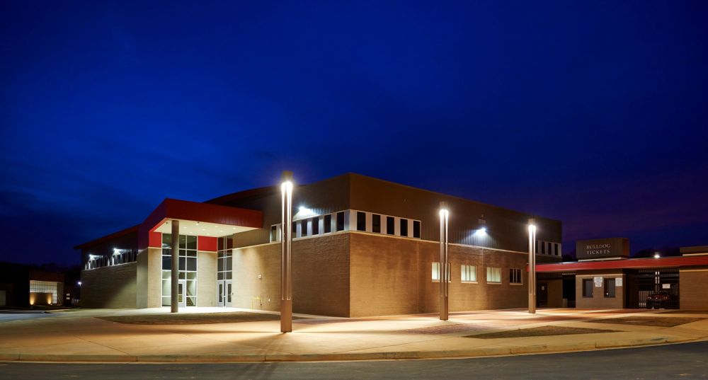 Building at night with exterior lights. Brown brick, red accents, and dark blue sky.
