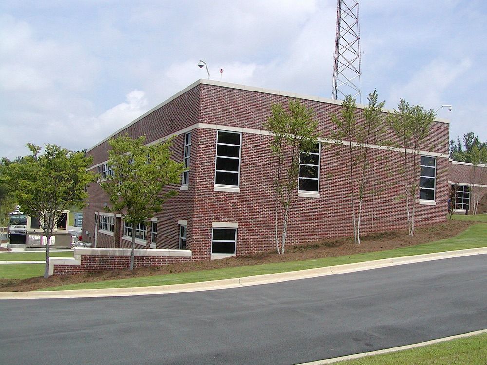 Brick building with multiple windows, small trees, and a radio tower on a slightly sloped lawn.