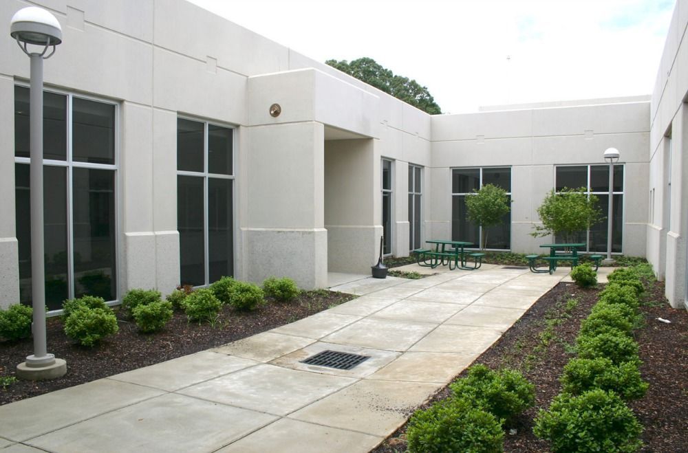 Courtyard with concrete walkway, landscaping, windows, and tables.