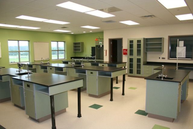 Empty science lab with green and black lab tables and cabinets. Green walls and beige floor.