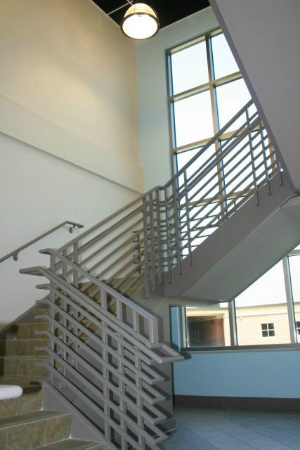 Staircase with metal railings, leading upwards towards large windows, bright light, modern building interior.