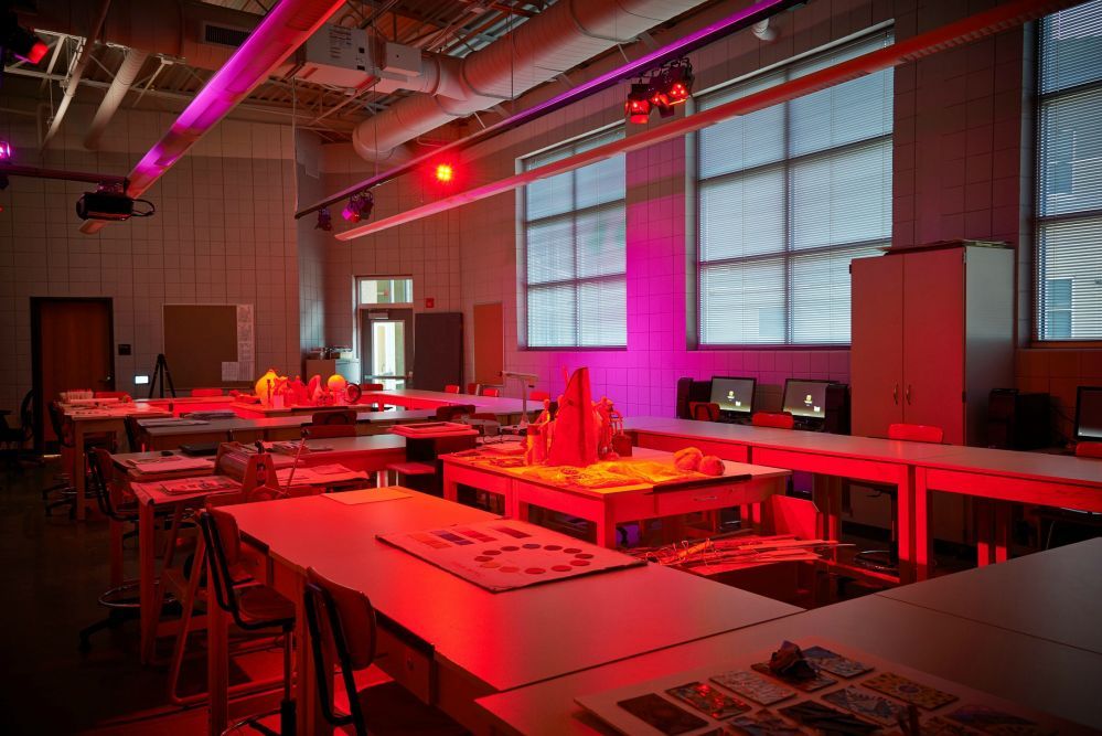 A brightly lit design studio with red and purple lighting, featuring work tables, models, and computers.