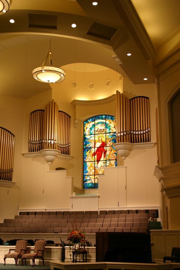 Interior church view with organ pipes, stained glass window, and rows of seating.