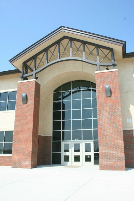 Entrance to a building with brick pillars, arched doorway, and large windows under a blue sky.